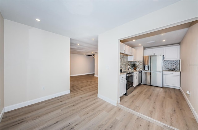 kitchen with appliances with stainless steel finishes, light wood-style floors, white cabinets, and tasteful backsplash