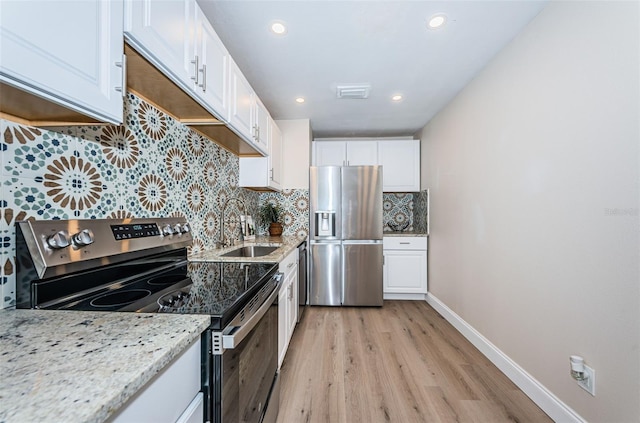 kitchen featuring stainless steel appliances, white cabinets, a sink, and light stone counters