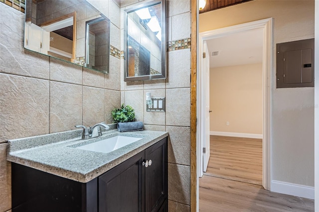 bathroom featuring wood finished floors, visible vents, vanity, tile walls, and electric panel