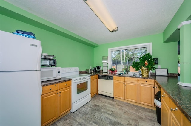 kitchen with white appliances, dark stone countertops, a textured ceiling, light wood-style floors, and a sink