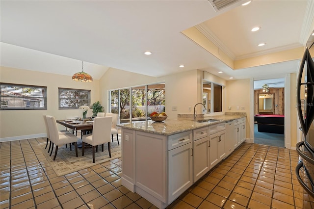 kitchen with light stone counters, a peninsula, a sink, white cabinetry, and decorative light fixtures