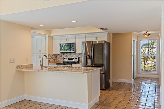 kitchen featuring light stone counters, appliances with stainless steel finishes, white cabinetry, a sink, and a peninsula