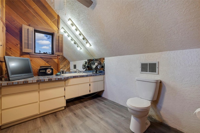 full bathroom featuring visible vents, a textured wall, vaulted ceiling, a textured ceiling, and wood finished floors