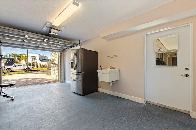 garage featuring a garage door opener, a sink, stainless steel refrigerator with ice dispenser, and baseboards