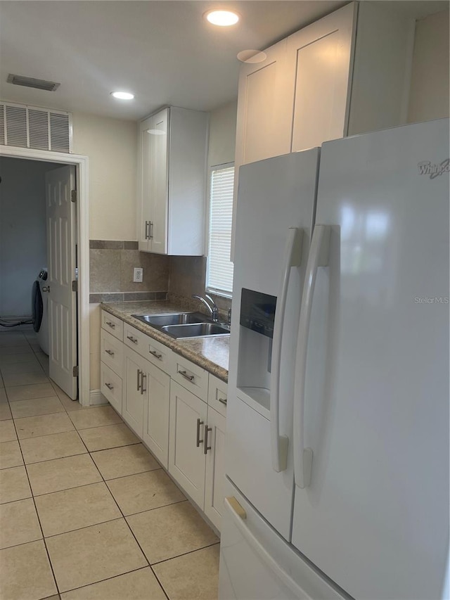 kitchen featuring white refrigerator with ice dispenser, white cabinetry, a sink, and light tile patterned flooring