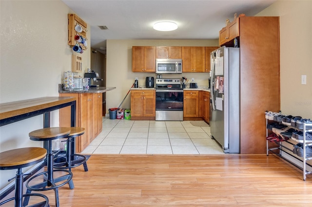 kitchen with a peninsula, appliances with stainless steel finishes, brown cabinetry, and light tile patterned flooring