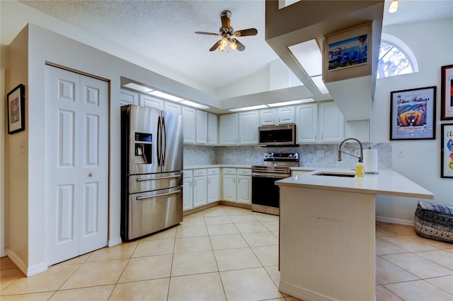 kitchen with light countertops, light tile patterned floors, a peninsula, stainless steel appliances, and a sink