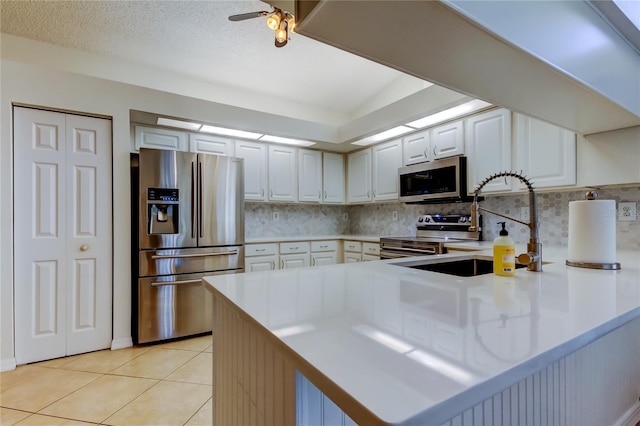 kitchen featuring tasteful backsplash, appliances with stainless steel finishes, a peninsula, light tile patterned flooring, and a sink