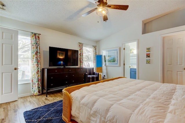 bedroom featuring lofted ceiling, wood finished floors, a textured ceiling, ensuite bath, and a ceiling fan