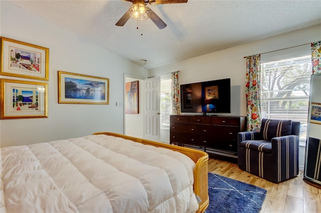 bedroom with ceiling fan, a textured ceiling, lofted ceiling, and light wood-style floors