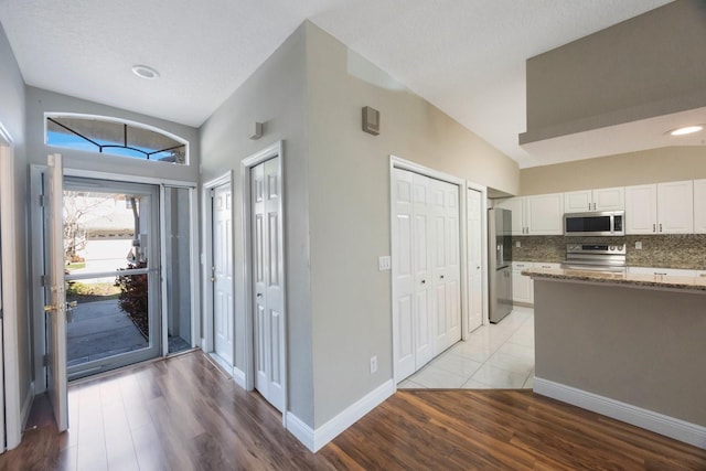 kitchen with tasteful backsplash, stone countertops, vaulted ceiling, stainless steel appliances, and white cabinetry