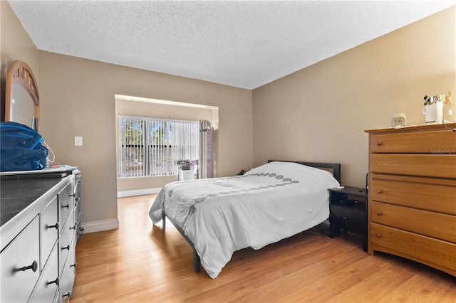 bedroom featuring light wood-type flooring, baseboards, and a textured ceiling