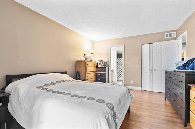 bedroom with baseboards, visible vents, light wood-style flooring, a textured ceiling, and a closet