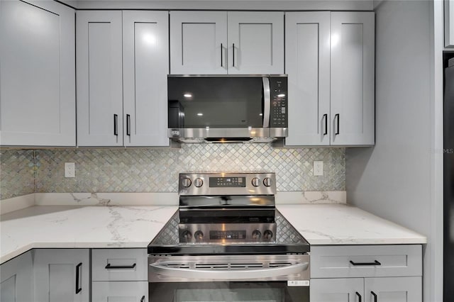 kitchen featuring tasteful backsplash, light stone counters, stainless steel appliances, and gray cabinetry