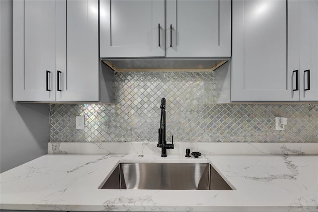 kitchen with tasteful backsplash, light stone counters, and a sink