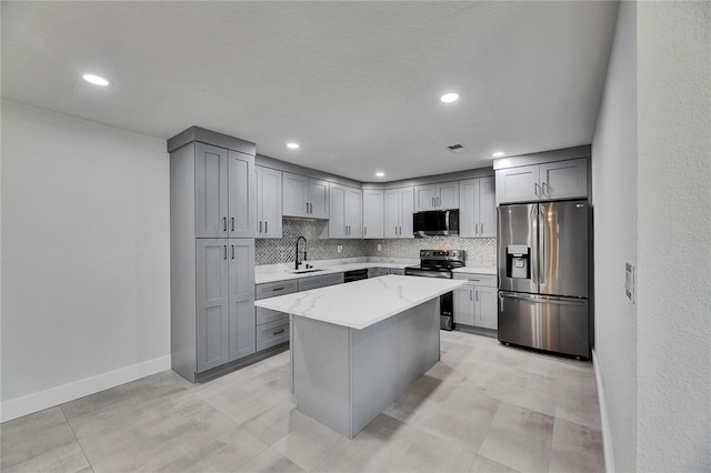 kitchen featuring appliances with stainless steel finishes, light stone counters, a sink, gray cabinetry, and backsplash