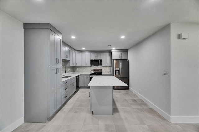 kitchen with stainless steel appliances, tasteful backsplash, gray cabinets, a sink, and light stone countertops