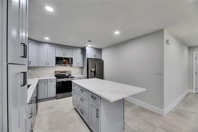 kitchen featuring a center island, stainless steel appliances, gray cabinets, decorative backsplash, and light stone countertops