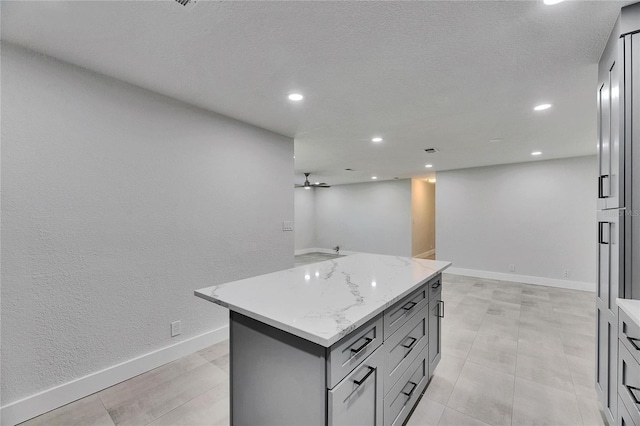 kitchen with light stone counters, recessed lighting, gray cabinetry, baseboards, and a center island