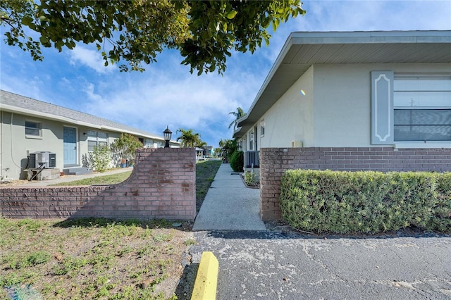 view of property exterior with brick siding, stucco siding, and central air condition unit