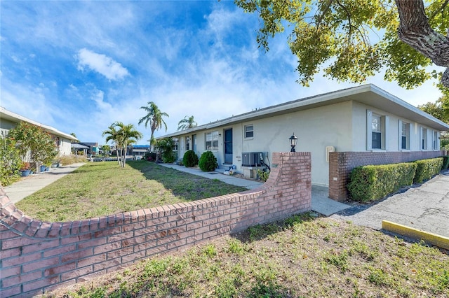 view of front of house featuring entry steps, brick siding, central air condition unit, a front lawn, and stucco siding