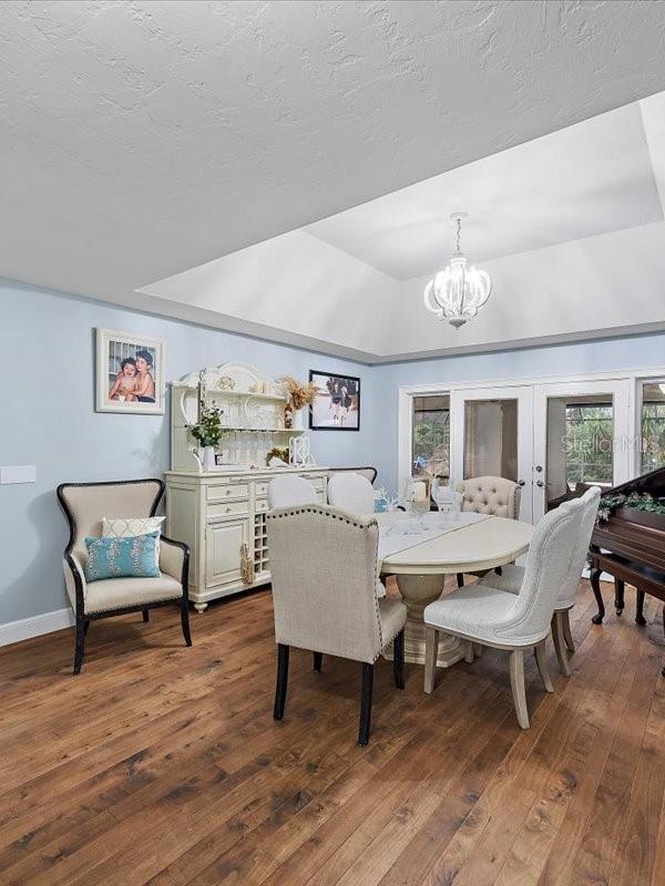 dining space with dark wood-style floors, a raised ceiling, a textured ceiling, and an inviting chandelier