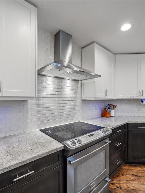 kitchen with stainless steel electric range oven, wall chimney exhaust hood, white cabinetry, and dark wood-style flooring