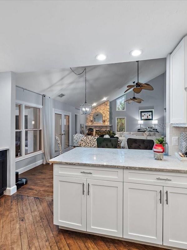 kitchen with white cabinets, dark wood finished floors, a peninsula, light stone countertops, and vaulted ceiling