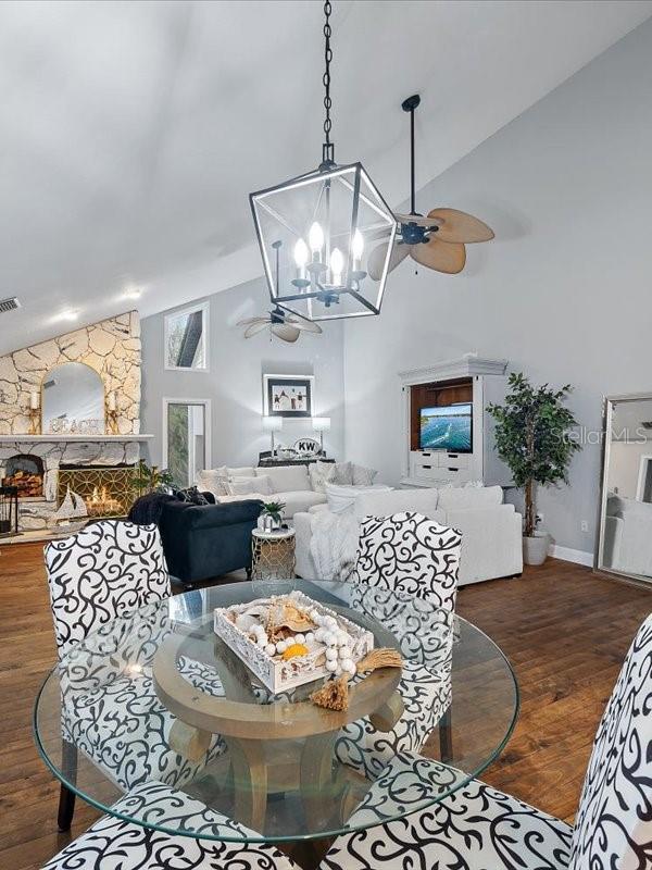 dining space with a fireplace, visible vents, wood finished floors, high vaulted ceiling, and ceiling fan with notable chandelier