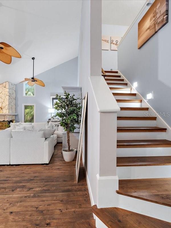 stairs with high vaulted ceiling, wood finished floors, and a ceiling fan