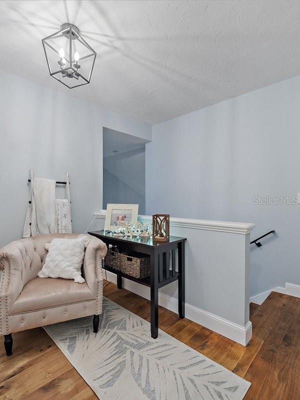 living area with a notable chandelier, hardwood / wood-style floors, a textured ceiling, an upstairs landing, and baseboards