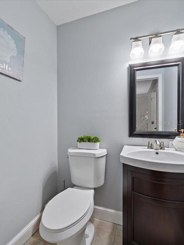 half bathroom featuring tile patterned flooring, baseboards, vanity, and toilet