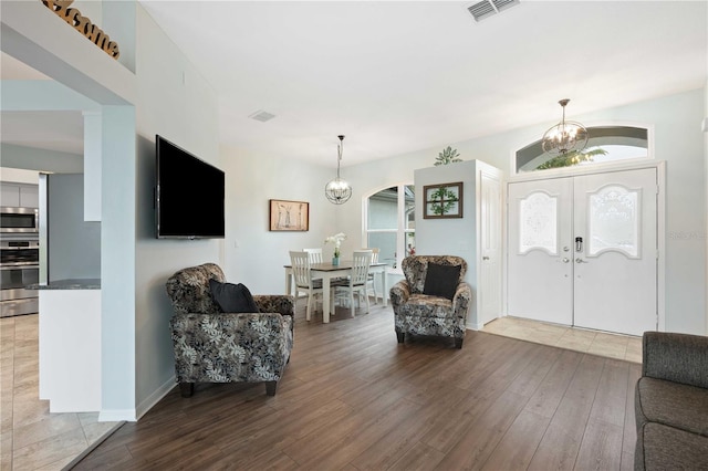 foyer with a wealth of natural light, wood finished floors, visible vents, and an inviting chandelier