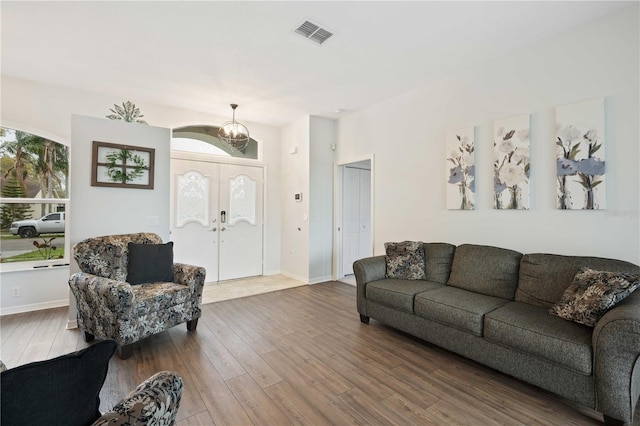 living area featuring baseboards, visible vents, wood finished floors, french doors, and a chandelier