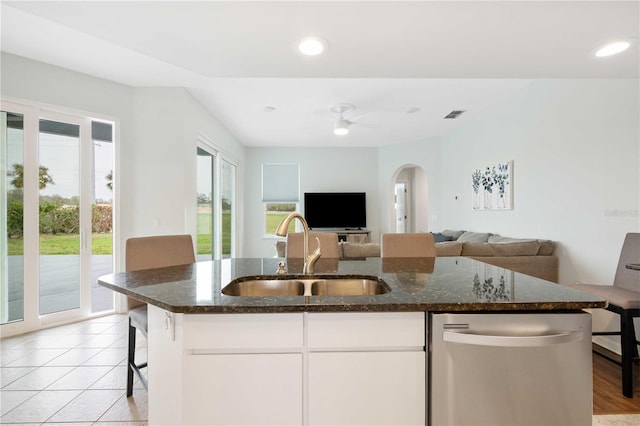 kitchen with arched walkways, stainless steel dishwasher, open floor plan, and a sink