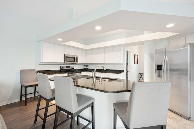 kitchen with white cabinets, dark stone counters, a breakfast bar area, appliances with stainless steel finishes, and a sink