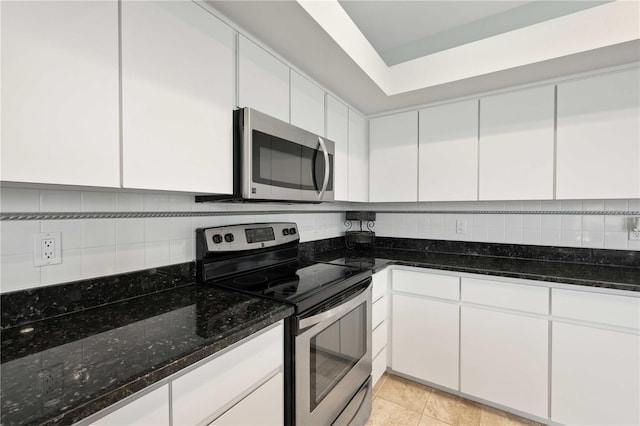 kitchen featuring stainless steel appliances, backsplash, white cabinets, light tile patterned flooring, and dark stone counters