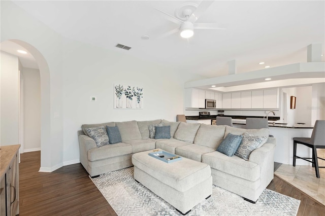 living area featuring a ceiling fan, arched walkways, visible vents, and dark wood finished floors