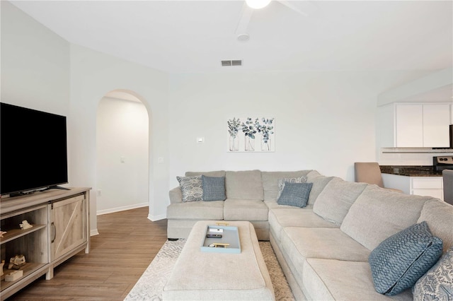 living room featuring baseboards, visible vents, arched walkways, ceiling fan, and light wood-style floors