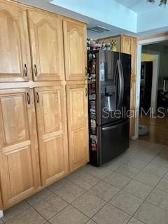 kitchen featuring light tile patterned floors, light brown cabinetry, and black refrigerator with ice dispenser