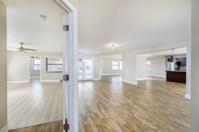 unfurnished living room featuring french doors, light wood finished floors, a ceiling fan, and baseboards