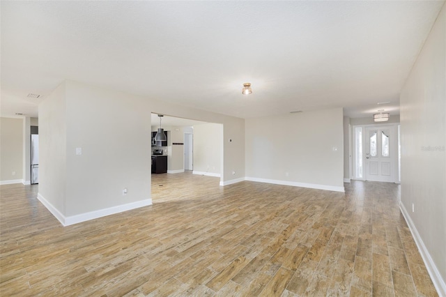 unfurnished living room with light wood-type flooring and baseboards