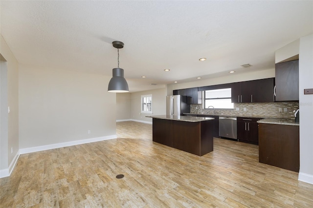 kitchen with appliances with stainless steel finishes, light wood-type flooring, a center island, and decorative backsplash