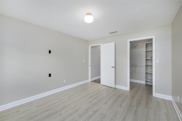 unfurnished bedroom featuring visible vents, baseboards, a spacious closet, a closet, and light wood-type flooring