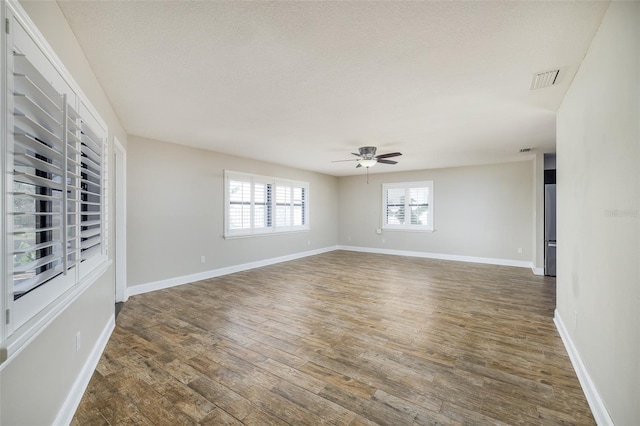 spare room with a ceiling fan, visible vents, baseboards, and wood finished floors