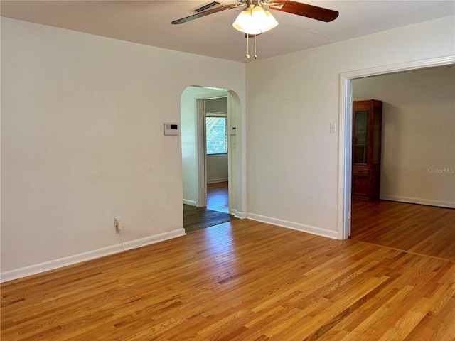 empty room with light wood-style floors, baseboards, arched walkways, and a ceiling fan