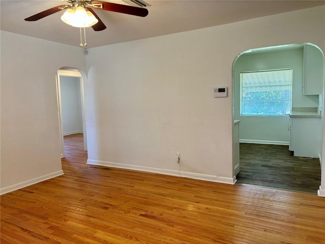 empty room featuring baseboards, arched walkways, ceiling fan, and wood finished floors