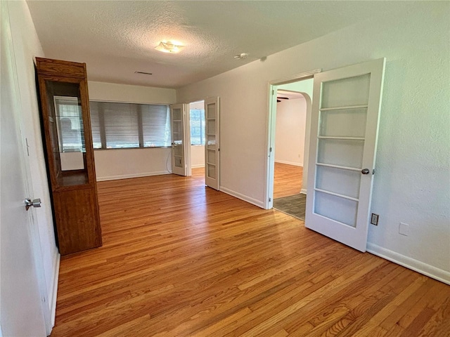 empty room with light wood finished floors, baseboards, arched walkways, and a textured ceiling