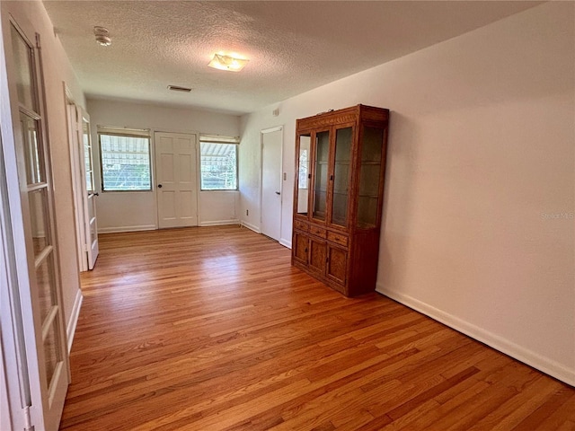 empty room with light wood-style flooring, a textured ceiling, visible vents, and baseboards