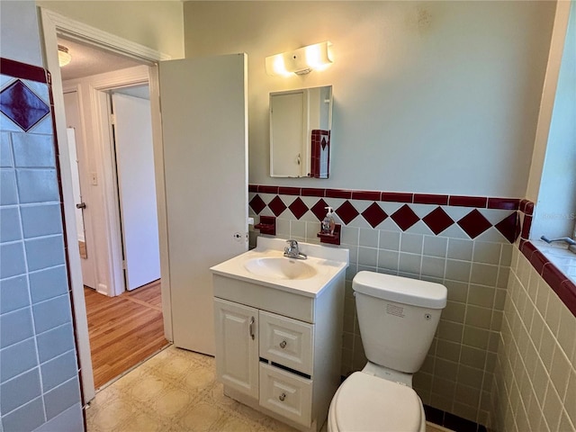 half bath featuring wainscoting, tile walls, toilet, and vanity